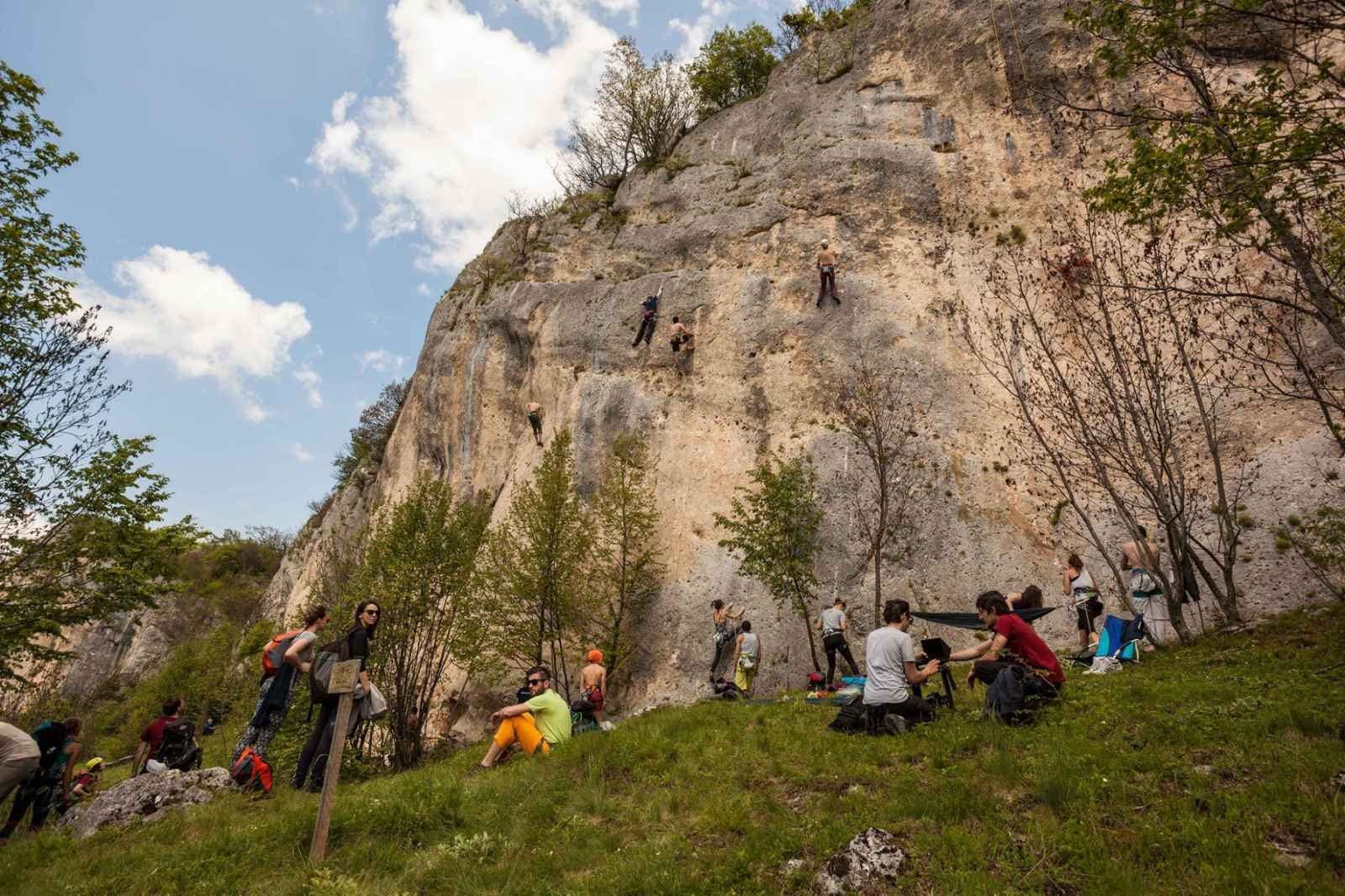 Penjači na krečnjačkoj stijeni iznad Pecke i grupa posjetilaca u travi ispod, tokom festivalskog dana