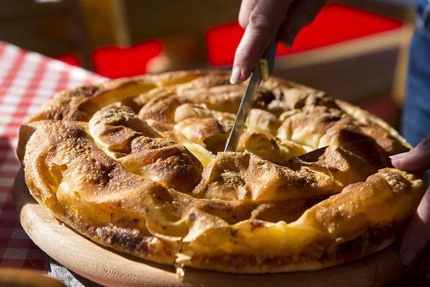 Domaća pita koja se reže na drvenoj dasci, na kariranom stolnjaku